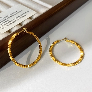 Detailed macro view of large gold hammered texture hoop earrings on a display stand