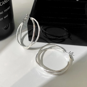 Close-up of interlocking silver hoop earrings featuring polished and frosted textures