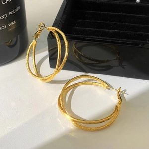 Close-up of golden interlocking hoop earrings with matte finish on black velvet display