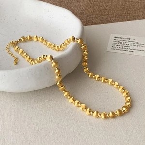 Detail of gold beaded necklace with lobster clasp on a ceramic plate with matte finish