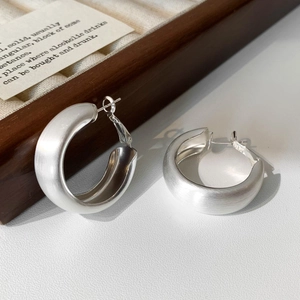 Detailed view of brushed s925 silver hoop earrings on a luxury wooden jewelry tray