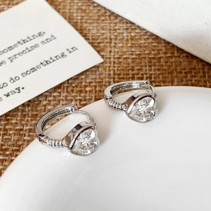 Detail shot of heart-shaped zircon earrings with textured silver-toned metal on white tray