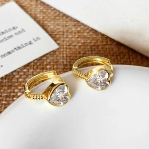 Close-up of heart-shaped zircon earrings in gold plating on a ceramic display