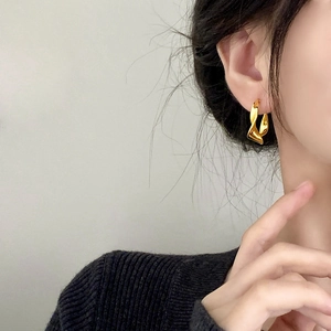 Elegant gold twisted geometric hoop earrings worn by a model in a minimalist style