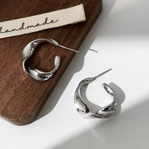 Detailed view of silver twist hoop earrings with a polished finish on wood surface