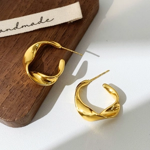 Close-up of golden twisted hoop earrings on a textured wood and white surface