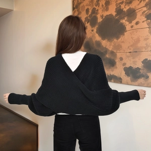 Detail of black knit shrug featuring a unique cross-back design and textured fabric finish