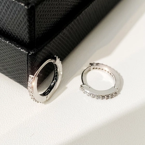 Detail of silver huggie earrings with cubic zirconia stones on white surface