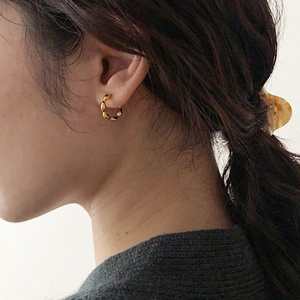 Detail of minimalist golden twisted hoop earring with polished braid texture on a model