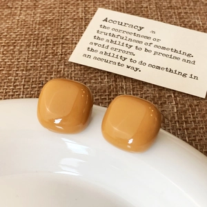 Detail of square amber-yellow resin stud earrings with a glossy finish on white ceramic