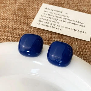 Close-up of deep blue resin square stud earrings with high-gloss finish on a ceramic plate
