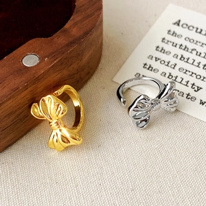 Minimalist bow-shaped open rings in gold and silver finish on a soft fabric surface
