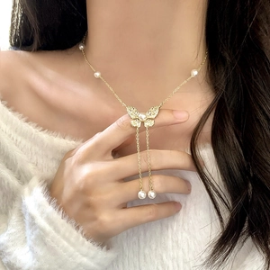 Elegante collana a farfalla dorata con perle e nappe indossata da una modella su maglia