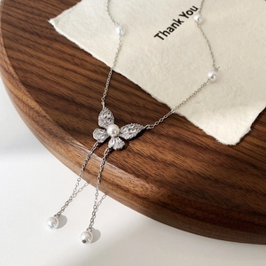 Dettaglio ravvicinato di una collana farfalla d'argento con perle su supporto in legno