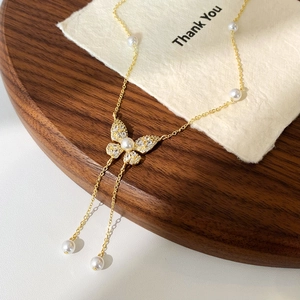 Dettaglio della collana a farfalla dorata con zirconi, perle e lunghe nappe su legno