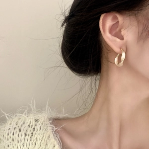 Close-up of model wearing matte gold twisted C-shaped earrings with a vintage French style