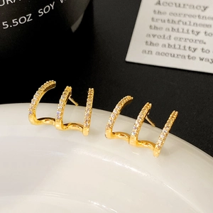 Macro detail of gold-plated curved claw earrings with three rows of micro-inlaid zircons