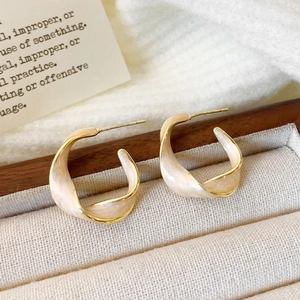 Detail of twisted gold earrings with pink enamel inlay on light wood background