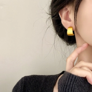 Minimalist matte gold curved stud earrings on model with brushed metal finish