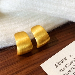 Detail of gold brushed matte metal texture on minimalist C-shaped geometric earrings