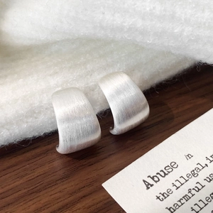 Macro shot of silver C-shaped earrings with brushed metallic texture on white fabric
