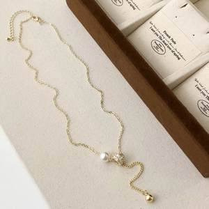 Elegant gold Y-shaped necklace featuring a white pearl pendant and zircon flower on beige linen