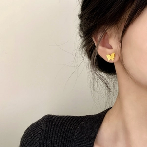Minimalist golden butterfly stud earrings with matte metal texture worn by a model