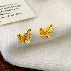 Macro detail of golden butterfly earrings with frosted texture on white knit fabric