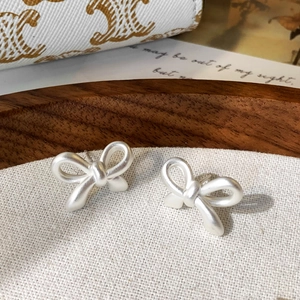 Detail shot of matte silver bow stud earrings featuring a textured frosted finish