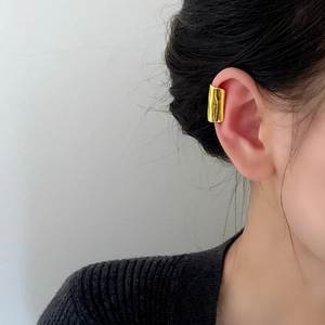 Minimalist gold ear cuff with irregular texture on a model's ear, sleek modern design
