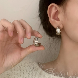 Silver wide hoop earrings with textured diagonal engraving shown on ear and finger
