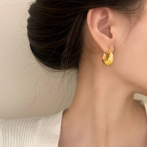 Elegant gold twisted hoop earrings with a textured spiral design on a model wearer