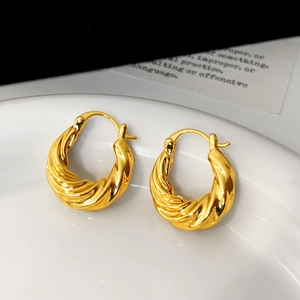 Close-up of twisted gold earrings with a polished spiral texture on a white plate