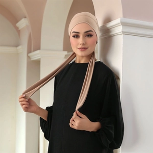 Detail of beige pleated hijab fabric and long decorative straps on a model in arcade