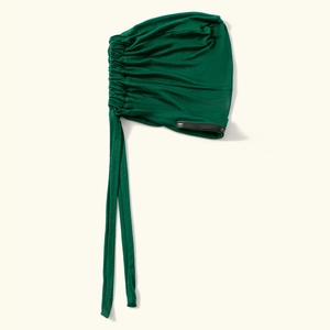 Dettaglio turbante elastico verde con pieghe laterali e lunghe cinghie regolabili.