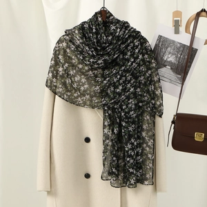 Detail view of a black floral voile scarf with purple flowers draped on a white coat