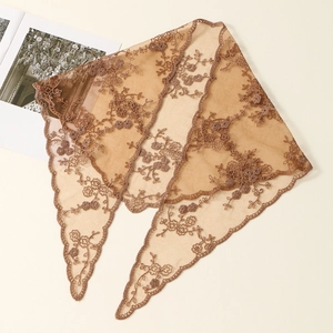 Detail of caramel lace triangle scarf with floral embroidery and wavy edges on art magazine