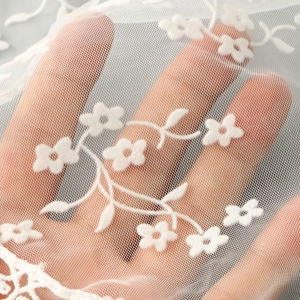 Detailed close-up of intricate white floral lace embroidery on semi-transparent mesh fabric