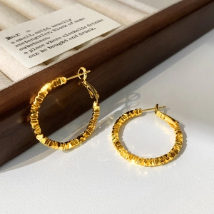 Macro detail of gold-plated hoop earrings featuring a unique hammered pleated texture design