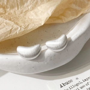 Detailed view of silver bean stud earrings with a brushed finish on ceramic plate