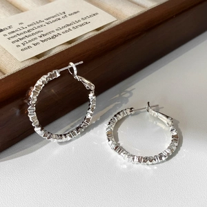 Macro detail of silver irregular hoop earrings with textured crinkle finish and snap closure