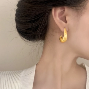 Boucles d'oreilles créoles dorées en C avec texture ondulée portée par un mannequin