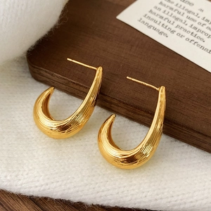 Détail de boucles d'oreilles dorées en U avec texture brossée sur carte bois