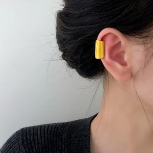 Minimalist gold ear cuff with textured wavy surface worn by a model on a grey background