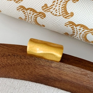 Macro detail of golden cylindrical metal ear cuff showing textured brushed finish