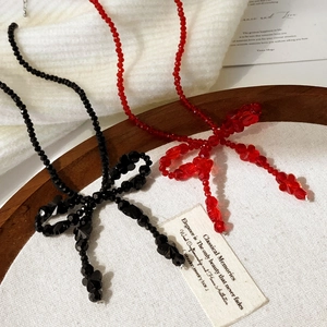 Collier élégant à perles avec nœud en noir et rouge présenté sur un plateau en bois