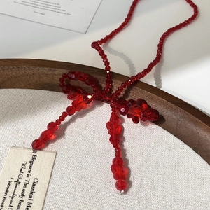 Vue détaillée du collier fait main en perles rouges avec pendentif noeud et pompons