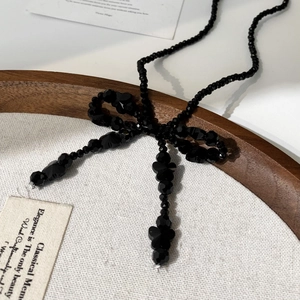 Collier élégant à perles noires avec nœud exposé sur un plateau en bois au style rétro chic
