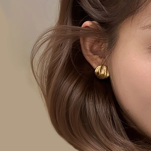 Boucles d'oreilles rondes dorées à texture plissée portées par un mannequin chic