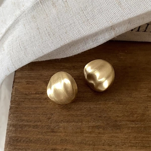 Détail macro de boucles d'oreilles dorées mates texturées sur fond de bois